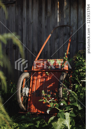 An old red wheelbarrow stands near an old wooden fence. An old red wheelbarrow stands near an old wooden fence. 121913764