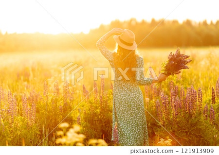 A beautiful woman with a bouquet of lupins, collects flowers, inhales fresh floral air. 121913909
