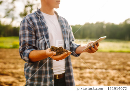 Farmer in a sunny field collects soil, checks its health using a digital tablet. Technology concept 121914072
