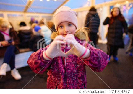 Child making heart shape with hands in winter gathering at festive location Child making heart shape with hands in winter gathering at festive location 121914257