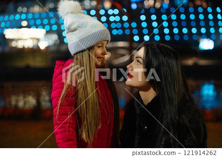 Smiling woman and girl enjoy a joyful moment together at night in a beautifully lit park Smiling woman and girl enjoy a joyful moment together at night in a beautifully lit park 121914262
