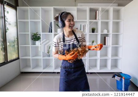 Joyful Woman Cleaning with Duster Wearing Headphones 121914447
