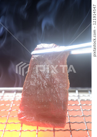 Grilling beef on a charcoal grill with smoke rising 121914547