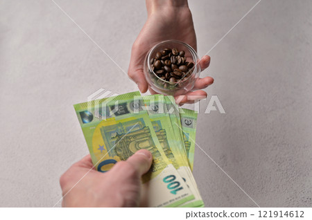 Close-up a man buys fresh aromatic coffee beans from a woman for 100 Euro paper cash banknotes, white background. Rising coffee prices in Europe Close-up a man buys fresh aromatic coffee beans from a woman for 100 Euro paper cash banknotes, white background. Rising coffee prices in Europe 121914612