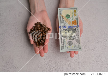 Top view fresh aromatic grain coffee and 100 American dollars paper cash banknote in a woman's hands, white background. Rising coffee prices in the world Top view fresh aromatic grain coffee and 100 American dollars paper cash banknote in a woman's hands, white background. Rising coffee prices in the world 121914613