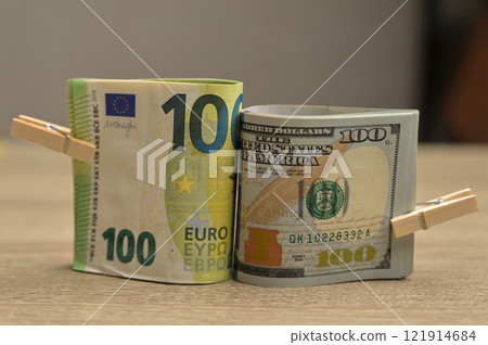 Rolls of 100 American and 100 Euro paper cash banknotes with a small clothespin on a wooden table background 121914684