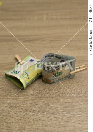 Rolls of 100 American and 100 Euro paper cash banknotes with a small clothespin on a wooden table background 121914685