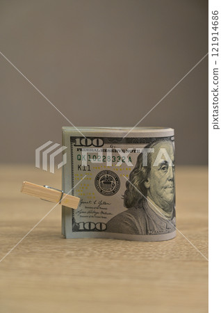 Roll of 100 American dollars paper cash banknotes with a small clothespin on a wooden table background, isolated 121914686