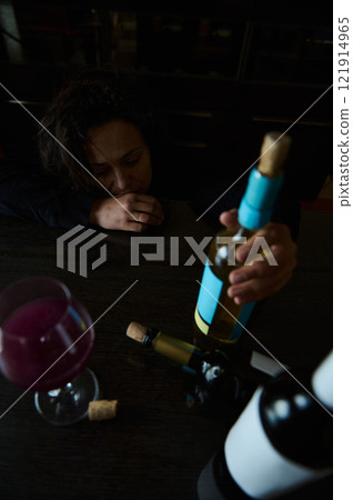 Person reflecting at a table with wine bottles and a glass in view Person reflecting at a table with wine bottles and a glass in view 121914965