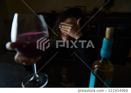Woman with wine at table, covering face in dark, contemplative mood Woman with wine at table, covering face in dark, contemplative mood 121914968