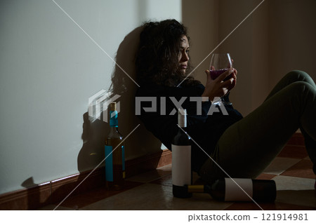 Thoughtful woman sitting in dim light surrounded by wine bottles Thoughtful woman sitting in dim light surrounded by wine bottles 121914981