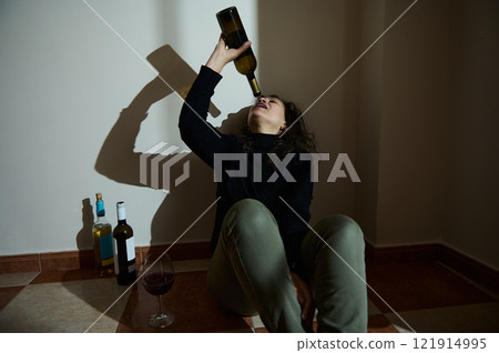 Person sitting in a corner with wine bottles showcasing personal struggle Person sitting in a corner with wine bottles showcasing personal struggle 121914995