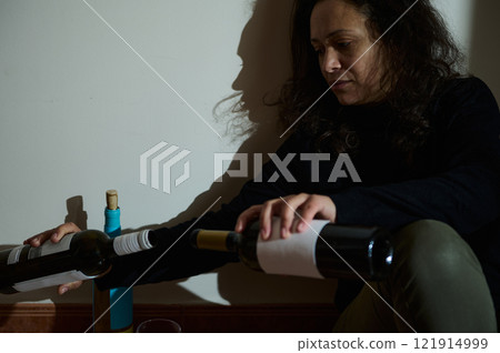 Woman sitting against a wall holding wine bottles in thoughtful contemplation Woman sitting against a wall holding wine bottles in thoughtful contemplation 121914999