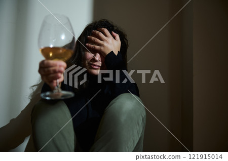 Person holding a wine glass sitting with distressed expression 121915014
