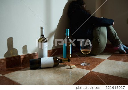 Person sitting against a wall with wine bottles in dim light Person sitting against a wall with wine bottles in dim light 121915017