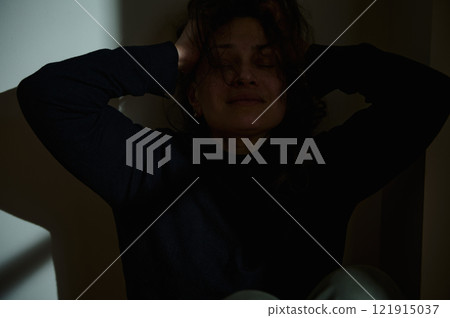 Woman distressed in low-light room holding her head 121915037