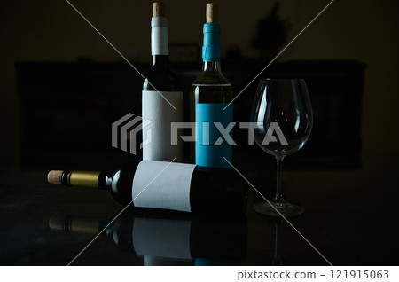 Three wine bottles and a glass on a reflective surface 121915063