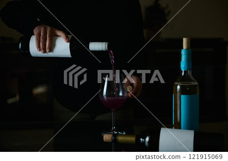 Pouring red wine into a glass with bottles arranged on a dark table Pouring red wine into a glass with bottles arranged on a dark table 121915069