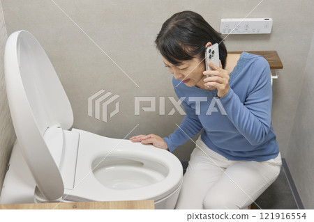 A woman calling a repairman in the bathroom 121916554