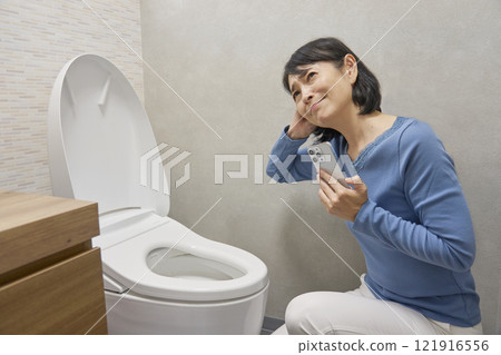 A woman checking repairman on her smartphone in the toilet A woman checking repairman on her smartphone in the toilet 121916556