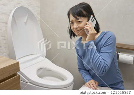 A woman calling a repairman in the bathroom A woman calling a repairman in the bathroom 121916557