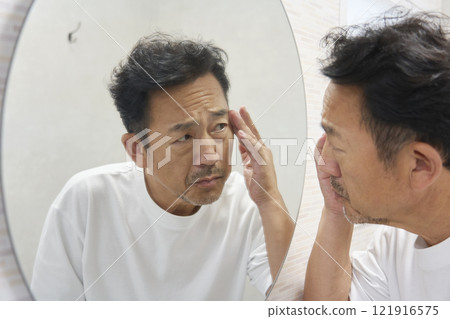 A man in his 50s worries about the corners of his eyes when looking in the mirror 121916575