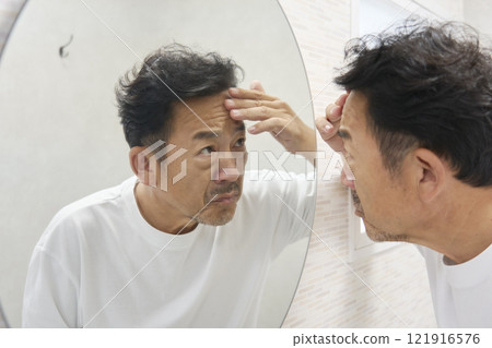 A man in his 50s worries about wrinkles on his forehead in the mirror A man in his 50s worries about wrinkles on his forehead in the mirror 121916576