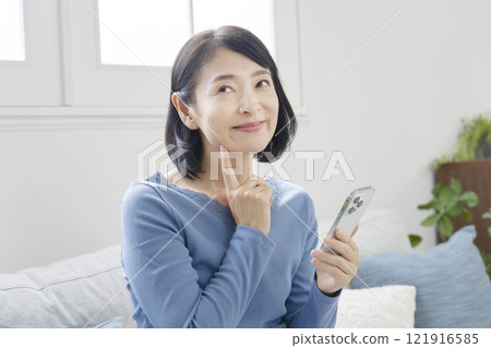 Middle-aged woman imagining with smartphone in living room 121916585