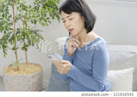 A middle-aged woman with a smartphone in her living room 121916591