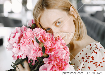 A beautiful young woman sitting in a cafe indoors and holding bouquet of flowers. Woman sitting on a sofa. Girl looking at camera. A beautiful young woman sitting in a cafe indoors and holding bouquet of flowers. Woman sitting on a sofa. Girl looking at camera. 121916625