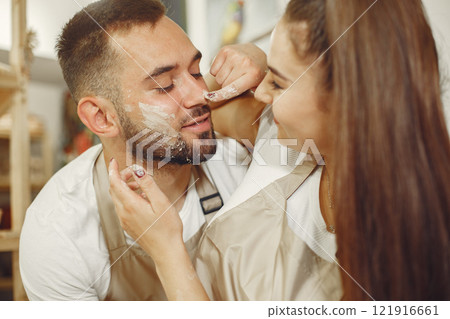 Mutual creative work. Young beautiful couple in casual clothes and aprons. People creating a bowl on a pottery wheel in a clay studio. 121916661