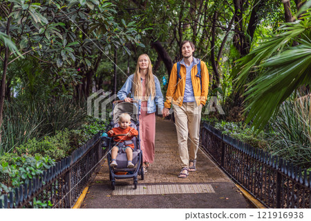 A married couple and their son in a stroller exploring lush streets of Condesa, Mexico City. Family adventure in a vibrant urban oasis. Travel, family bonding, and urban greenery concept in Latin 121916938