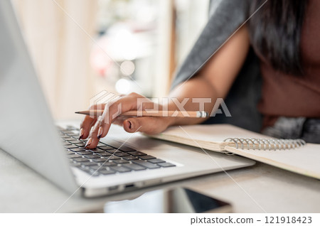 A close-up of a woman works remotely from a coffee shop, typing on a laptop keyboard. A close-up of a woman works remotely from a coffee shop, typing on a laptop keyboard. 121918423
