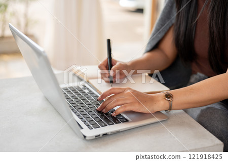 A close-up of a woman works remotely from a coffee shop, typing on a laptop keyboard. A close-up of a woman works remotely from a coffee shop, typing on a laptop keyboard. 121918425
