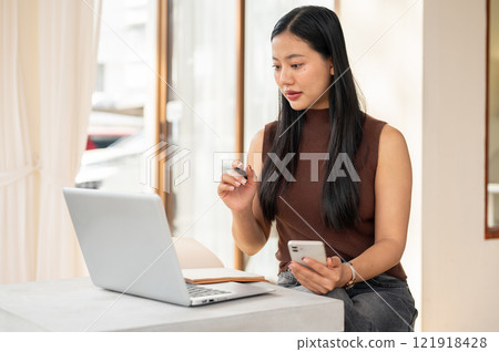 A beautiful Asian woman working remotely from a coffee shop in the morning, working on her laptop. 121918428