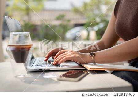 A woman working on her laptop at a cafe in the morning, seated at an outdoor table. A woman working on her laptop at a cafe in the morning, seated at an outdoor table. 121918469