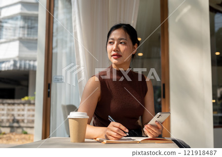 A beautiful, thoughtful Asian woman looks to the side, pondering something while relaxing at a cafe. A beautiful, thoughtful Asian woman looks to the side, pondering something while relaxing at a cafe. 121918487