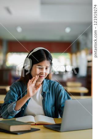Young Woman Using Laptop with Headphones in Library for Online Learning or Video Call, Engaged in Digital Education or Remote Work 121919274