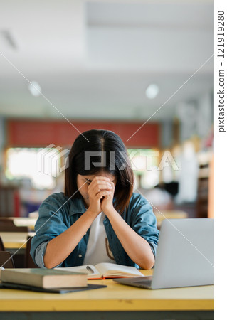 Student Deep in Thought at Library Desk with Open Books and Laptop in Bright Study Environment 121919280