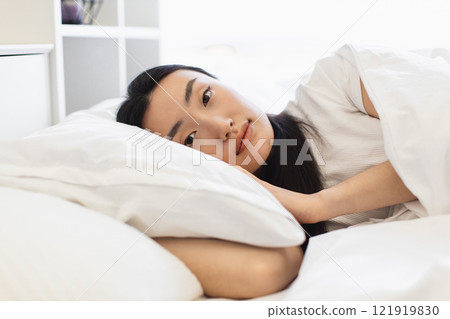 Asian woman lying comfortably in bed, showcasing relaxation and tranquility. Soft lighting highlights calm morning ambiance. Female adult enjoying restful moment, conveying peaceful. Asian woman lying comfortably in bed, showcasing relaxation and tranquility. Soft lighting highlights calm morning ambiance. Female adult enjoying restful moment, conveying peaceful. 121919830