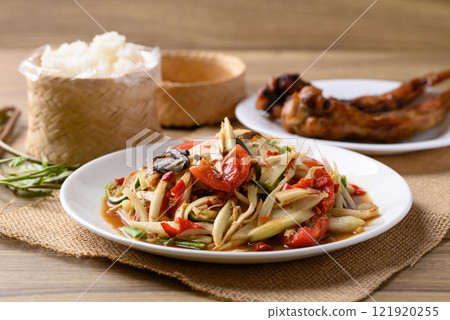 Spicy papaya salad (Som Tum) eating with sticky rice and grilled chicken wing on wooden table, 121920255