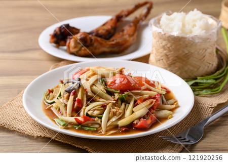 Spicy papaya salad (Som Tum) eating with sticky rice and grilled chicken wing on wooden table 121920256
