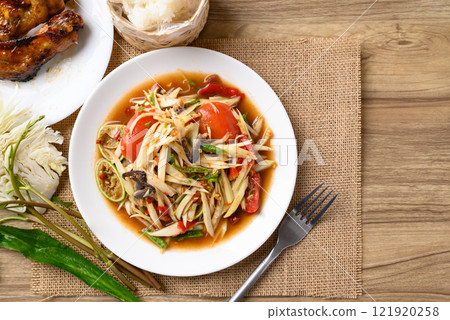 Spicy papaya salad (Som Tum) eating with sticky rice and grilled chicken wing on wooden table 121920258
