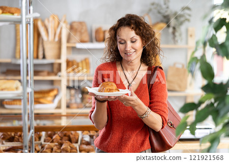 European woman customer holding disposable plate with burger in bakery 121921568