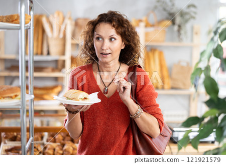 Happy female customer tries delicious bocadillo in bakery interior Happy female customer tries delicious bocadillo in bakery interior 121921579
