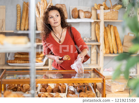 Woman putting croissants into plastic bag in bakery 121921580