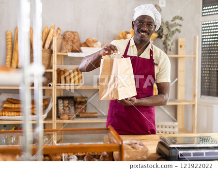 Smiling male baker presenting a takeaway paper bag Smiling male baker presenting a takeaway paper bag 121922022