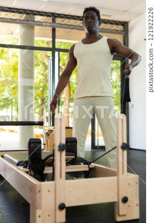 African american man doing pilates exercises lying on pilates workout machines closeup African american man doing pilates exercises lying on pilates workout machines closeup 121922226