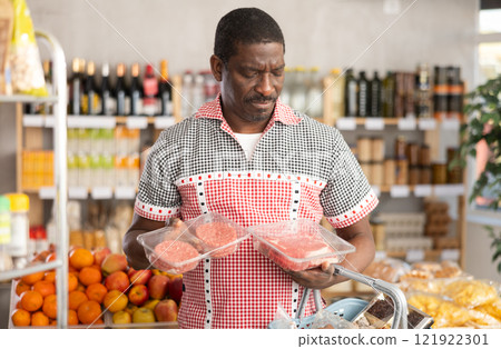 African man in store took raw beef steaks and hamburger cutlet, choose meat ware African man in store took raw beef steaks and hamburger cutlet, choose meat ware 121922301