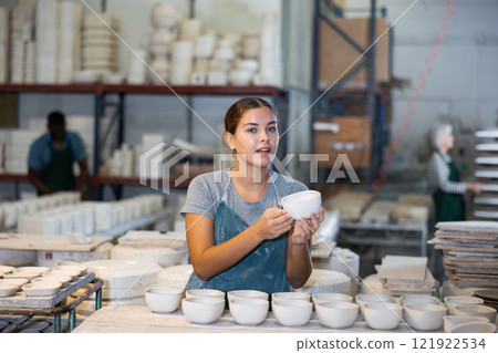 Girl ceramist arranging new bowls in workshop Girl ceramist arranging new bowls in workshop 121922534